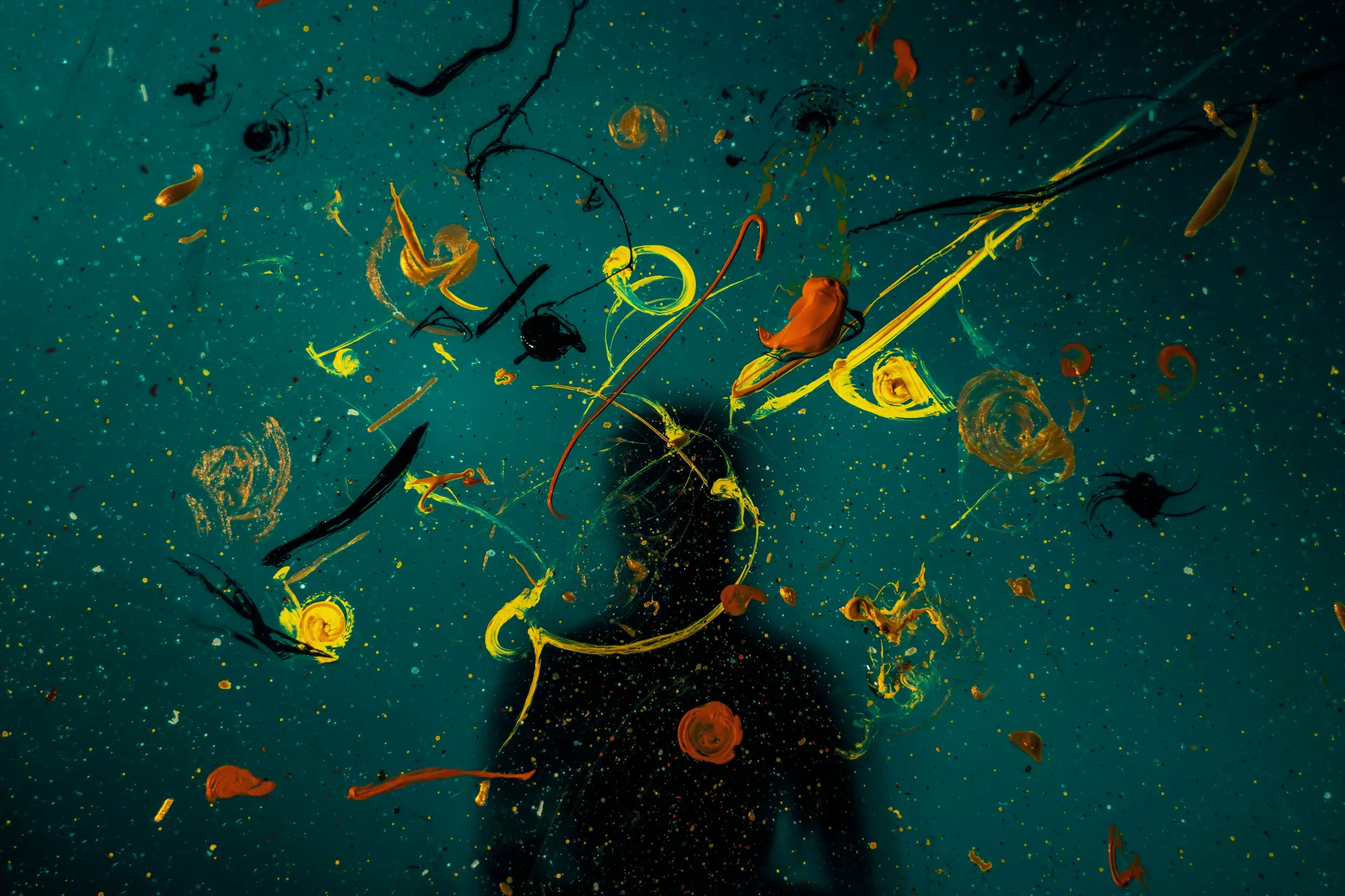 Paint spots and swirls on a board or opaque glass, with a person's shadow.