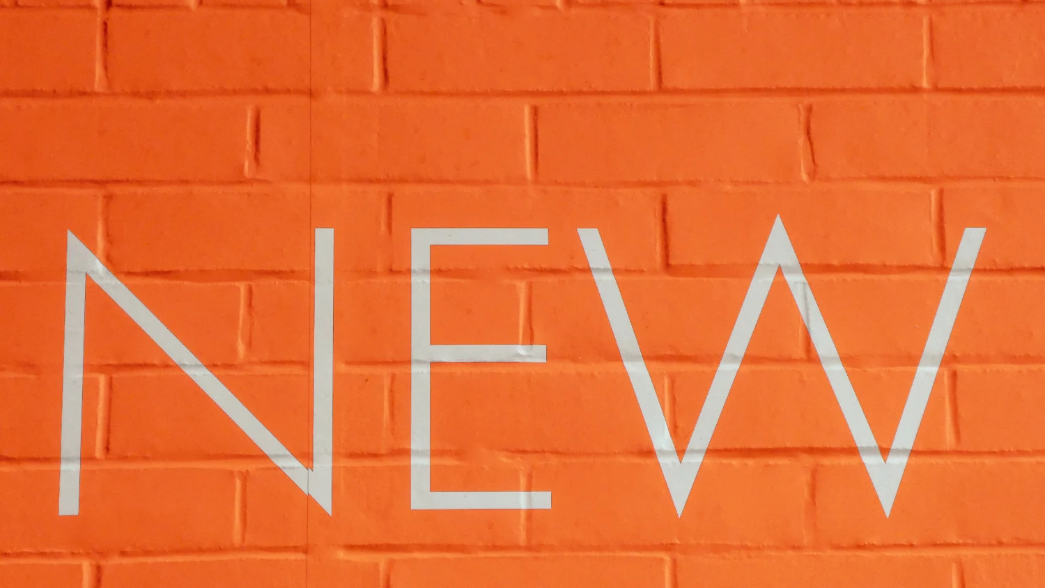 An orange brick wall with the word 'New' on it.